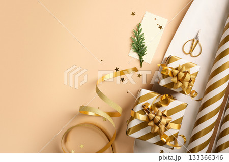 Christmas gift wrapping with golden and white striped wrapping paper, ribbon, scissors, and small gift boxes on beige backdrop. Copy space. 133366346