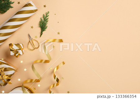 Items for Christmas gift wrapping. Golden and white striped wrapping paper, ribbon, scissors on beige backdrop. Copy space. Items for Christmas gift wrapping. Golden and white striped wrapping paper, ribbon, scissors on beige backdrop. Copy space. 133366354