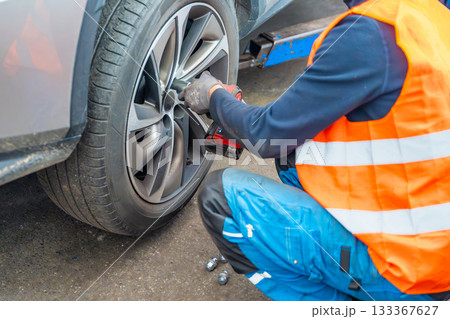Mechanic using an impact wrench to remove lug nuts from a car wheel. Seasonal tire change and professional car service in preparation for winter. 133367627