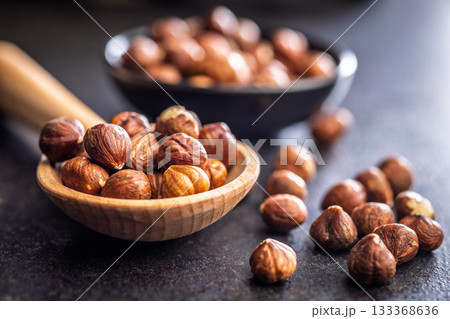 Peeled hazelnut kernels on wooden spoon on black table. Peeled hazelnut kernels on wooden spoon on black table. 133368636
