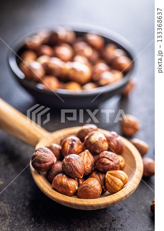 Peeled hazelnut kernels on wooden spoon on black table. Peeled hazelnut kernels on wooden spoon on black table. 133368637
