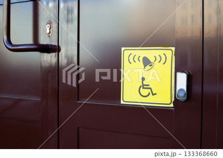 Yellow square sticker with symbol of person in wheelchair and bell next to the panel. Button for calling for assistance at the entrance of building for people with disabilities Yellow square sticker with symbol of person in wheelchair and bell next to the panel. Button for calling for assistance at the entrance of building for people with disabilities 133368660