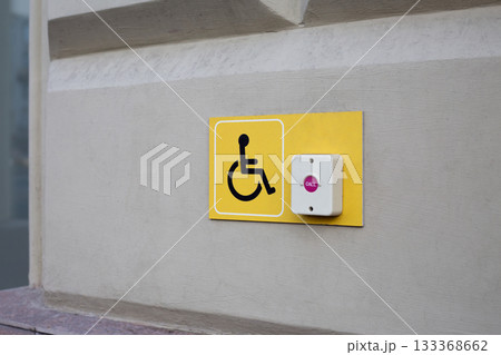 Yellow plastic panel to attract the attention of people with disabilities. Visible panel with wheelchair symbol and call button for assistance at the entrance to accessible building Yellow plastic panel to attract the attention of people with disabilities. Visible panel with wheelchair symbol and call button for assistance at the entrance to accessible building 133368662