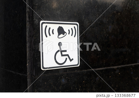 Black wall with white sign of person in wheelchair and bell symbol symbolizes accessible environment for people with physical injuries. Concept for assisting people with limited mobility Black wall with white sign of person in wheelchair and bell symbol symbolizes accessible environment for people with physical injuries. Concept for assisting people with limited mobility 133368677