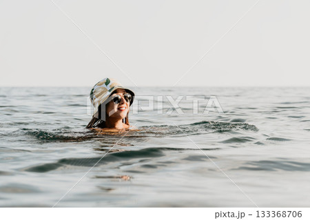 Woman Swimming Ocean Sunglasses Hat - A woman in sunglasses and a hat swims in the ocean. 133368706