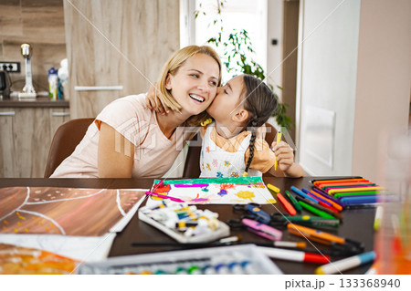 Cute girl kisses her mother while they both work on vibrant art projects 133368940