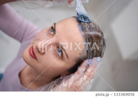 Hairdresser applying hair dye to woman with brush in salon 133369056