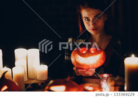 Young woman making Halloween pumpkin Jack-o-lantern with candles in dark 133369229