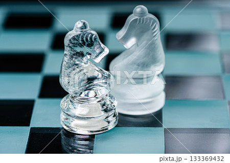 two opponent glass chess knights on a glass chess board, black background two opponent glass chess knights on a glass chess board, black background 133369432