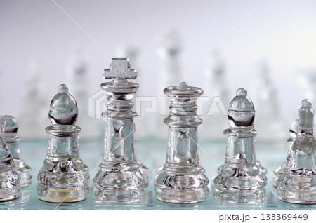 glass, transparent chess pieces on a checkerboard, selective focus, close-up, isolated on light 133369449