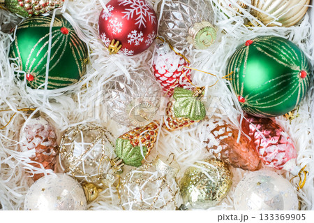 Top-down close-up of white box filled with assorted glass Christmas tree ornaments in red, green, gold and white. Christmas preparation, storing Christmas tree decorations, texture 133369905