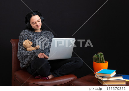 teenager female sitting with laptop, headphones and teddy bear, learning remotely online from home 133370231