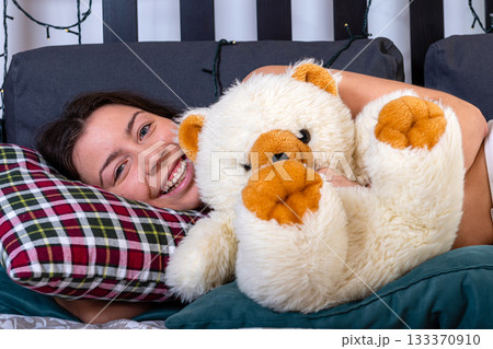attractive smiling happy young woman hugging her teddy bear at bedroom 133370910