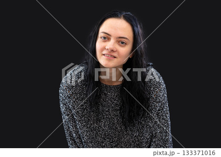 portrait of young woman with long dark hair wearing gray knitted sweater over black background 133371016