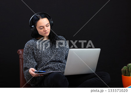 focused young freelance woman sitting with laptop and headphones, working remotely online from home 133371020