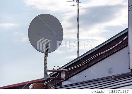 一軒家の屋根に取り付けられた灰色をした小型の衛星放送用パラボラアンテナ 一軒家の屋根に取り付けられた灰色をした小型の衛星放送用パラボラアンテナ 133371187