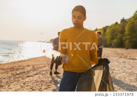 Earth day. Volunteers activists team collects garbage cleaning of beach coastal zone. Woman puts plastic bottle trash in garbage bag on ocean shore. Environmental conservation coastal zone cleaning 133371978