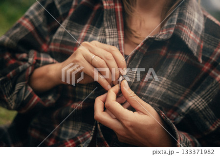 rustic morning routine with cozy clothing, closeup of hands buttoning warm flannel in outdoor 133371982