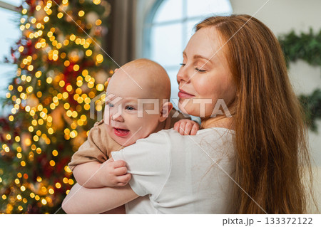 Merry Christmas Xmas. Happy family mother newborn baby child hugging bonding near Christmas tree at home. Mom girl kid celebrating Christmas New Year enjoying winter holidays together. Family moments Merry Christmas Xmas. Happy family mother newborn baby child hugging bonding near Christmas tree at home. Mom girl kid celebrating Christmas New Year enjoying winter holidays together. Family moments 133372122