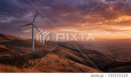 Wind turbines stand tall on rolling hills during a vibrant sunset in a rural landscape 133372129