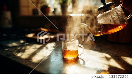 Warm tea being poured into a glass cup on a sunny kitchen countertop Warm tea being poured into a glass cup on a sunny kitchen countertop 133372293