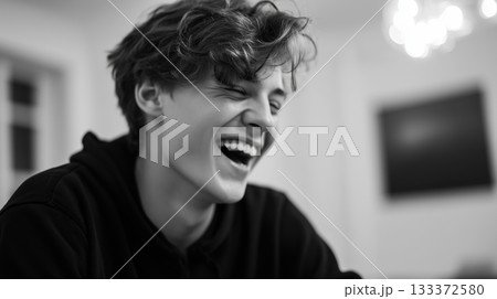 Young man laughs joyfully in a cozy indoor setting during evening gathering with friends 133372580