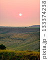 The sun sets over rolling steppe hills, painting the sky in soft orange hues 133374238