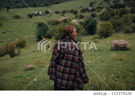 solitary figure moves toward distant mountains, an introspective woman traverses open grassland at solitary figure moves toward distant mountains, an introspective woman traverses open grassland at 133374326