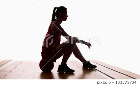 Basketball player resting on ball after training in silhouette lighting 133375734