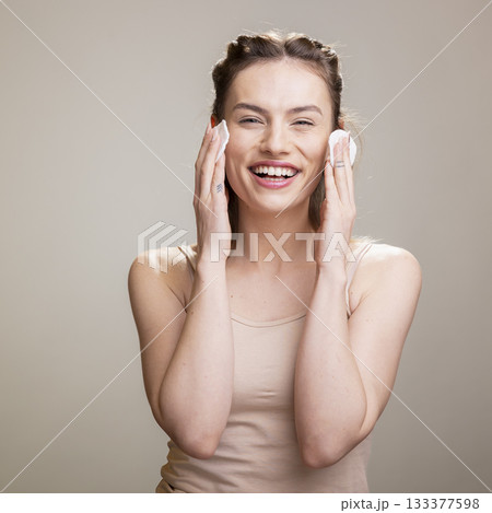 Portrait of a graceful female model using cotton pads to gently remove makeup. Her happy expression and natural beauty promoting a nourishing night routine with micellar water for wellness. Portrait of a graceful female model using cotton pads to gently remove makeup. Her happy expression and natural beauty promoting a nourishing night routine with micellar water for wellness. 133377598