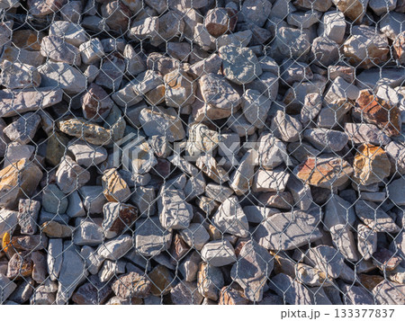 Gabion stone wall construction close up. New stone fence in wire grid, iron cage with rocks 133377837