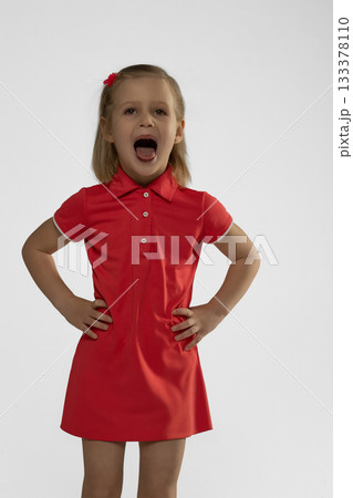 little blonde girl is in a bright studio wearing a red dress. She shows a big smile and appears to be having fun during the session full of energy and joy. little blonde girl is in a bright studio wearing a red dress. She shows a big smile and appears to be having fun during the session full of energy and joy. 133378110