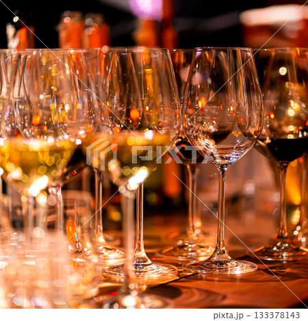 Elegant scene of wine being poured into glasses aligned in a row, showcasing the rich colors and graceful flow of the liquid, set against a dark, warm background, ideal sophisticated dining settings 133378143