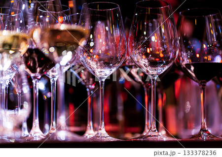 Elegant scene of wine being poured into glasses aligned in a row, showcasing the rich colors and graceful flow of the liquid, set against a dark, warm background, ideal sophisticated dining settings 133378236