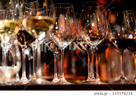 Elegant scene of wine being poured into glasses aligned in a row, showcasing the rich colors and graceful flow of the liquid, set against a dark, warm background, ideal sophisticated dining settings Elegant scene of wine being poured into glasses aligned in a row, showcasing the rich colors and graceful flow of the liquid, set against a dark, warm background, ideal sophisticated dining settings 133378238