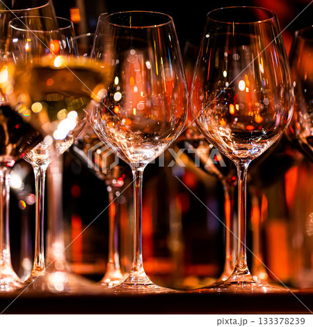 Elegant scene of wine being poured into glasses aligned in a row, showcasing the rich colors and graceful flow of the liquid, set against a dark, warm background, ideal sophisticated dining settings 133378239