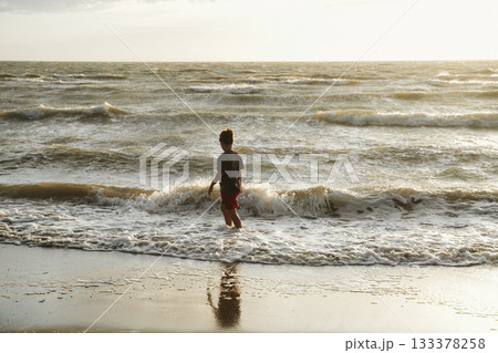 Child Enjoying Waves at the Beach During Sunset 133378258