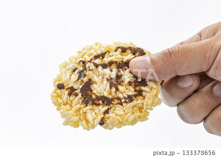 Hand Holding a Crispy Rice Snack Drizzled with Dark simmered cane sugar Against a White Background in Close-Up Detail Hand Holding a Crispy Rice Snack Drizzled with Dark simmered cane sugar Against a White Background in Close-Up Detail 133378656