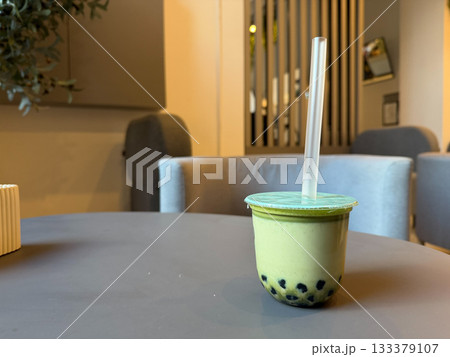 Creamy matcha bubble tea in a sealed plastic cup sits on a cafe table, with soft indoor lighting and a neutral modern interior in the background Creamy matcha bubble tea in a sealed plastic cup sits on a cafe table, with soft indoor lighting and a neutral modern interior in the background 133379107