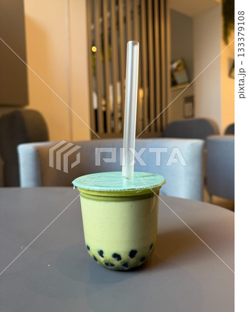 Creamy matcha bubble tea in a sealed plastic cup sits on a cafe table, with soft indoor lighting and a neutral modern interior in the background Creamy matcha bubble tea in a sealed plastic cup sits on a cafe table, with soft indoor lighting and a neutral modern interior in the background 133379108