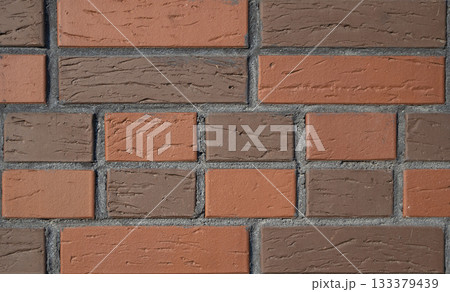 Close up view of brick wall features alternating pattern of red orange and brown bricks. The surface has rough, textured appearance with distinct mortar lines. Background for interior design projects. Close up view of brick wall features alternating pattern of red orange and brown bricks. The surface has rough, textured appearance with distinct mortar lines. Background for interior design projects. 133379439