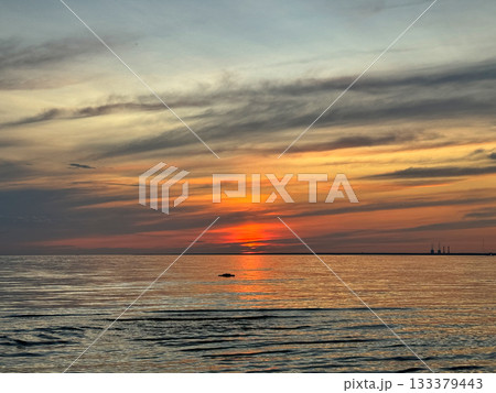 Vibrant sunset over calm sea with dramatic orange and gray clouds. Reflection of sun creating golden path on water surface. The view is peaceful and vast. 133379443
