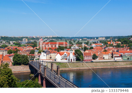 Cityscape panoramic view shows the old town of Kaunas, Lithuania. Red tiled rooftops and historic buildings line the Nemunas River and bridge in summer sunny day. Famous travel destination. 133379446