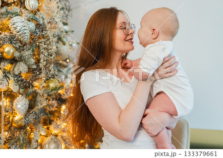 Merry Christmas Xmas. Happy family mother newborn baby child hugging bonding near Christmas tree at home. Mom girl kid celebrating Christmas New Year enjoying winter holidays together. Family moments 133379661