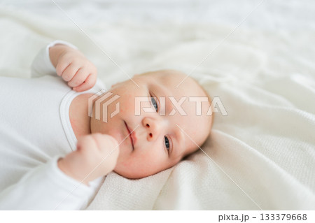 Happy baby. Cute little newborn girl with smiling face lying on bed in bedroom. Infant baby resting playing lying down on white blanket at home. Motherhood happy child childcare concept Happy baby. Cute little newborn girl with smiling face lying on bed in bedroom. Infant baby resting playing lying down on white blanket at home. Motherhood happy child childcare concept 133379668