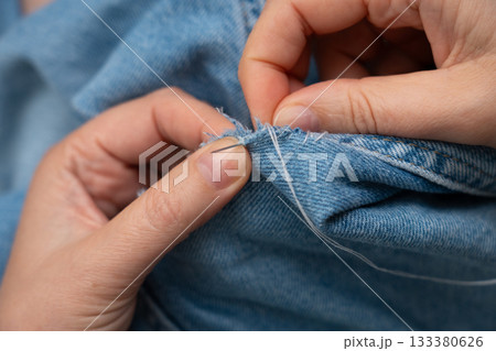 Woman mends jeans by hand with needle 133380626
