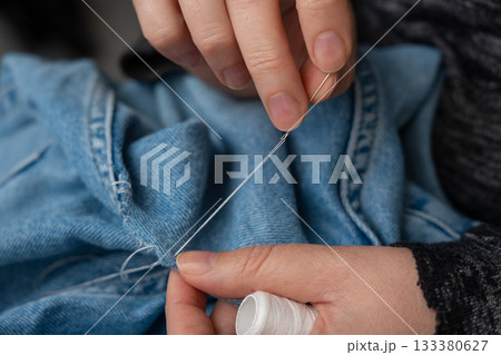 Woman mends jeans by hand with needle 133380627