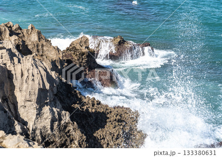 Waves of the Atlantic Ocean crash against sharp volcanic coastal rocks on a sunny day 133380631