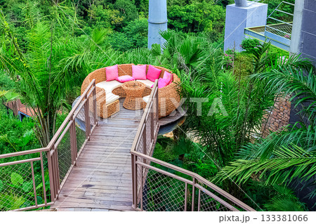 A circular rattan seating area with pink cushions against a backdrop of lush tropical plants in Yanoda Park, Sanya, Hainan, China A circular rattan seating area with pink cushions against a backdrop of lush tropical plants in Yanoda Park, Sanya, Hainan, China 133381066