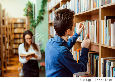 Male and female college students looking for necessary books in library. Historical department of library. Students studying at historical faculty prepare for classes 133381236